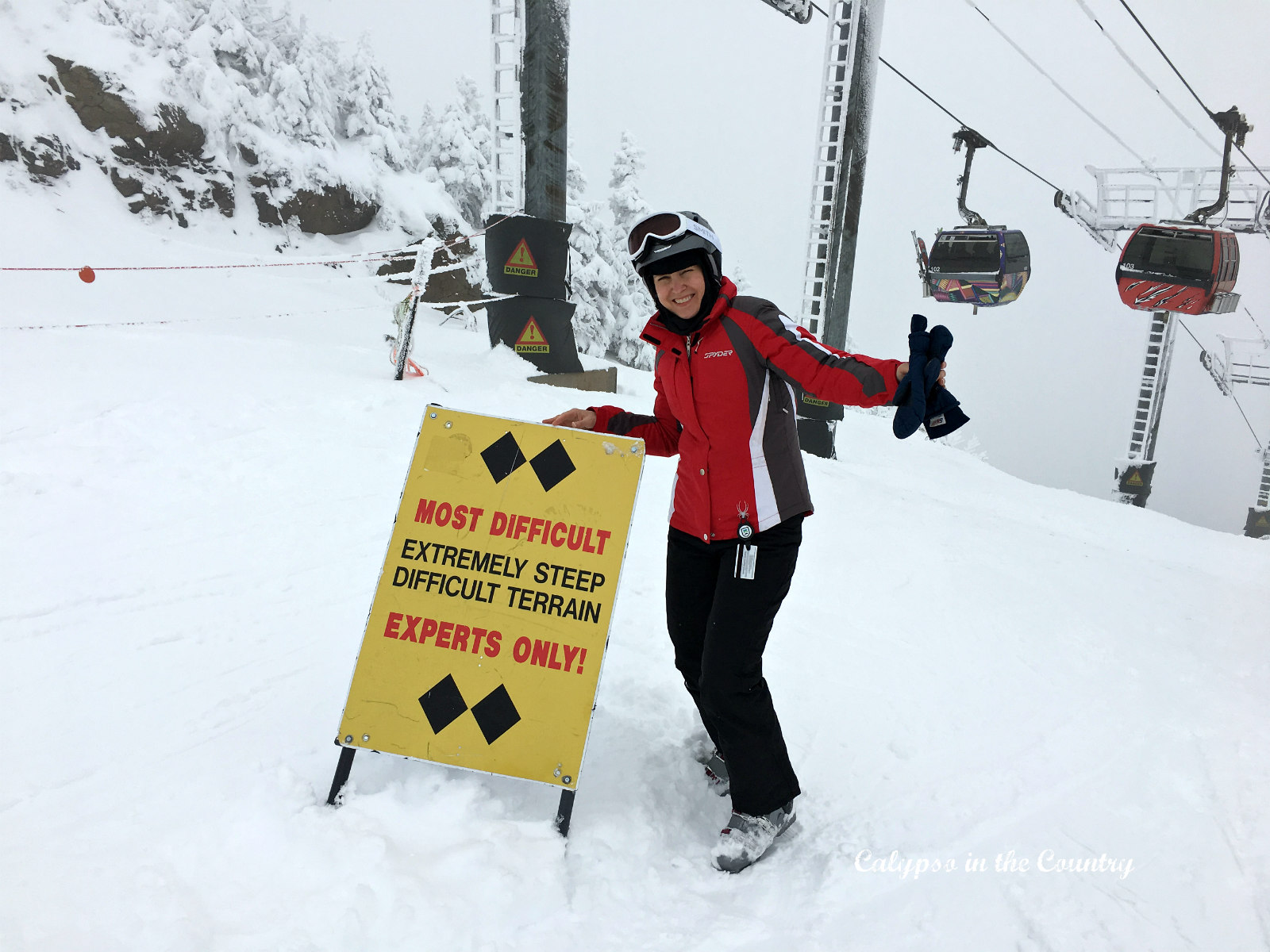 Skier in red jacket on expert trail with gondolas in background