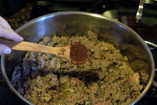 Chili powder being added to cooked ground beef in  the skillet. 