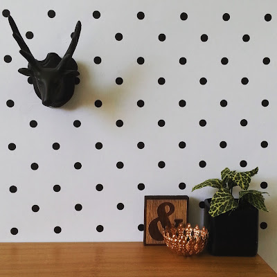 Modern dolls' house miniature scene with a black stag head mounted on a spotty wall behind a desk displaying a plant in a black pot, a bronze bowl and a wooden ampersand plaque.