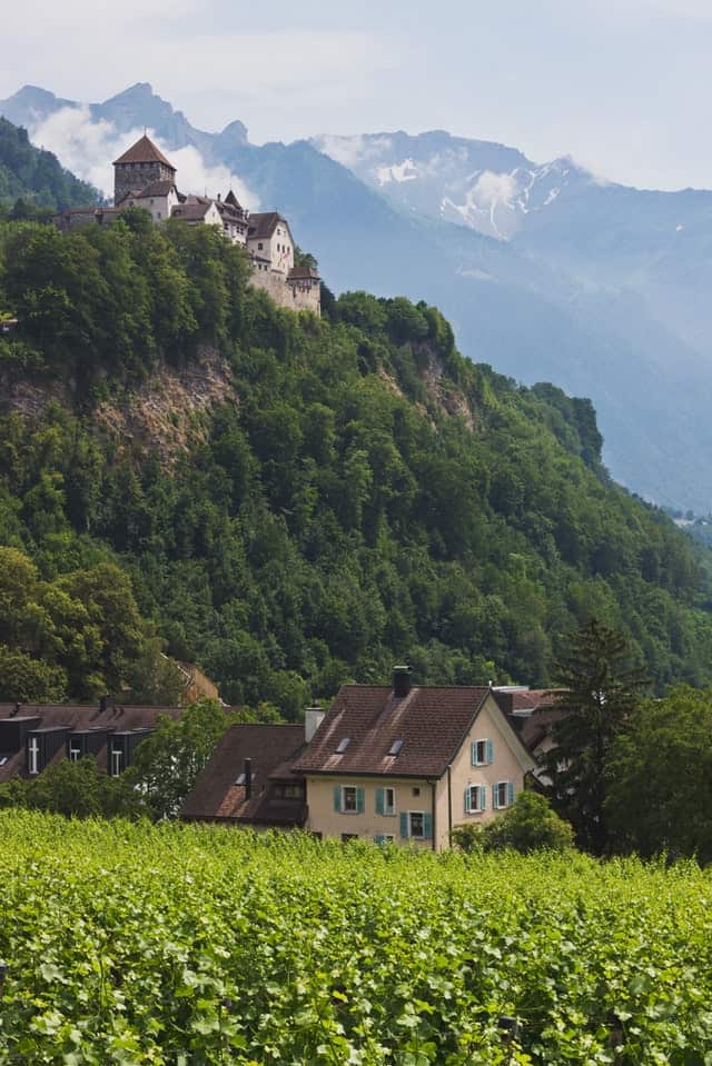 A small cottage surrounded by greens with Vaduz Castle in the background in Liechtenstein