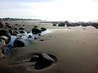 Large rocks on a New Zealand black-sand beach at low tide.