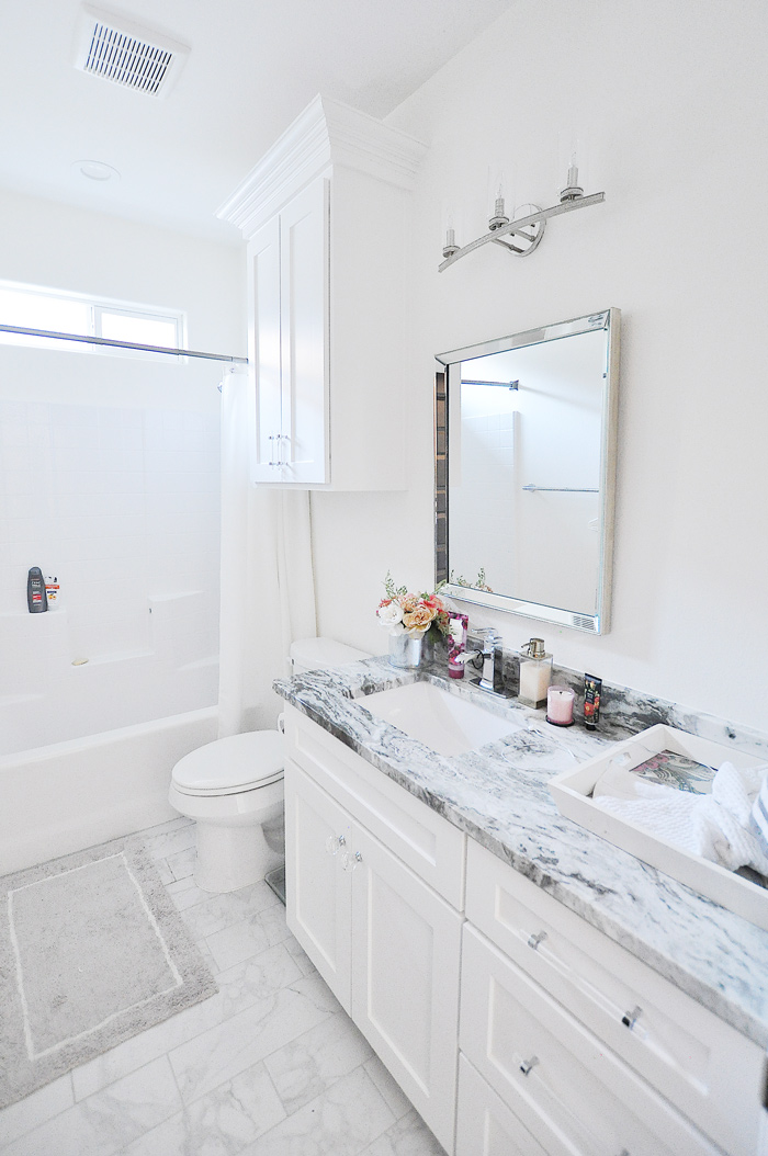 Regrets from our new construction home in Corpus Christi A crisp white guest bathroom with shaker cabinets, crystal lighting, lucite hardware and a marble tile floor with white walls.