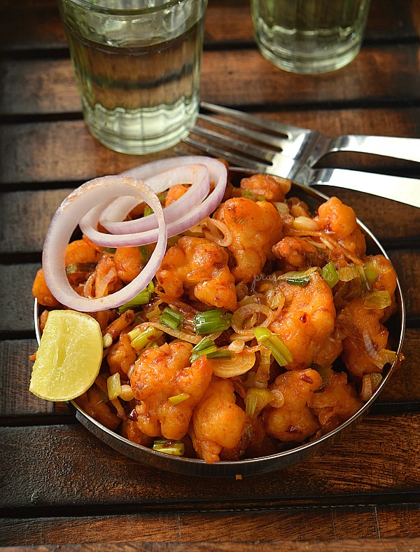 A stainless steel plate serve with spicy Indian street food Gobi Manchurian along with lemon wedges and onion rings