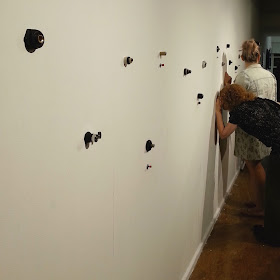 A woman peering into one of several small holes in an art gallery wall.