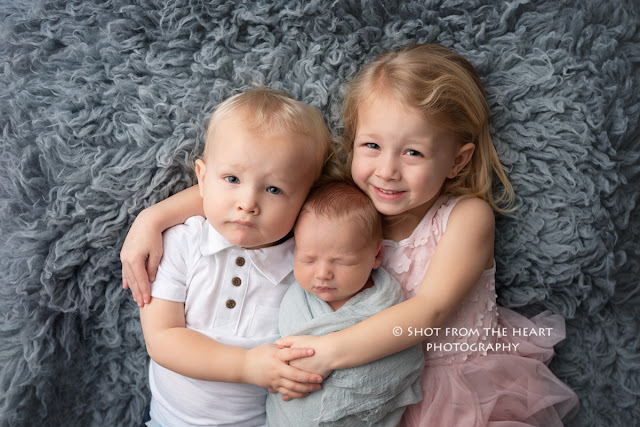 newborn with brother and sister pose, smiling, laying on flokati