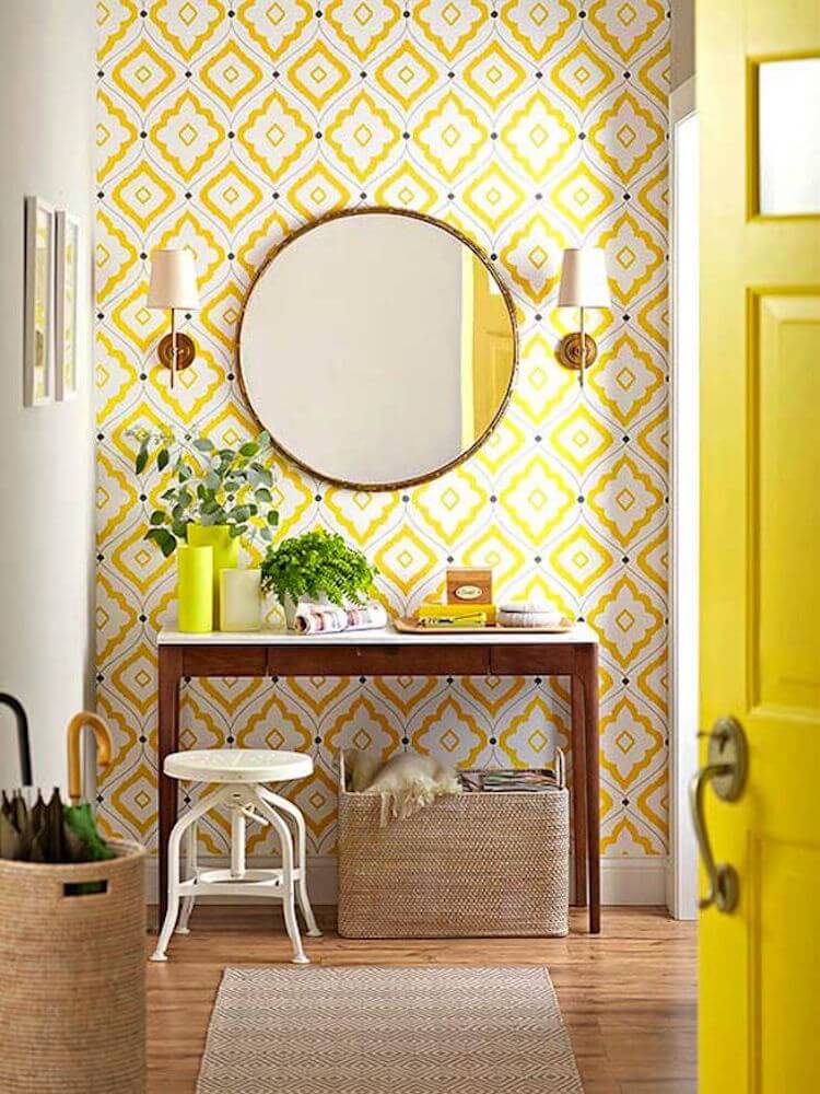 baño con papel pintado de motivos geométricos en color amarillo y gran espejo circular