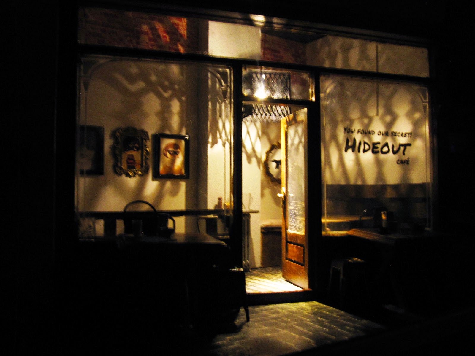 Exterior of a modern dolls' house miniature cafe at night, with the interior light up.