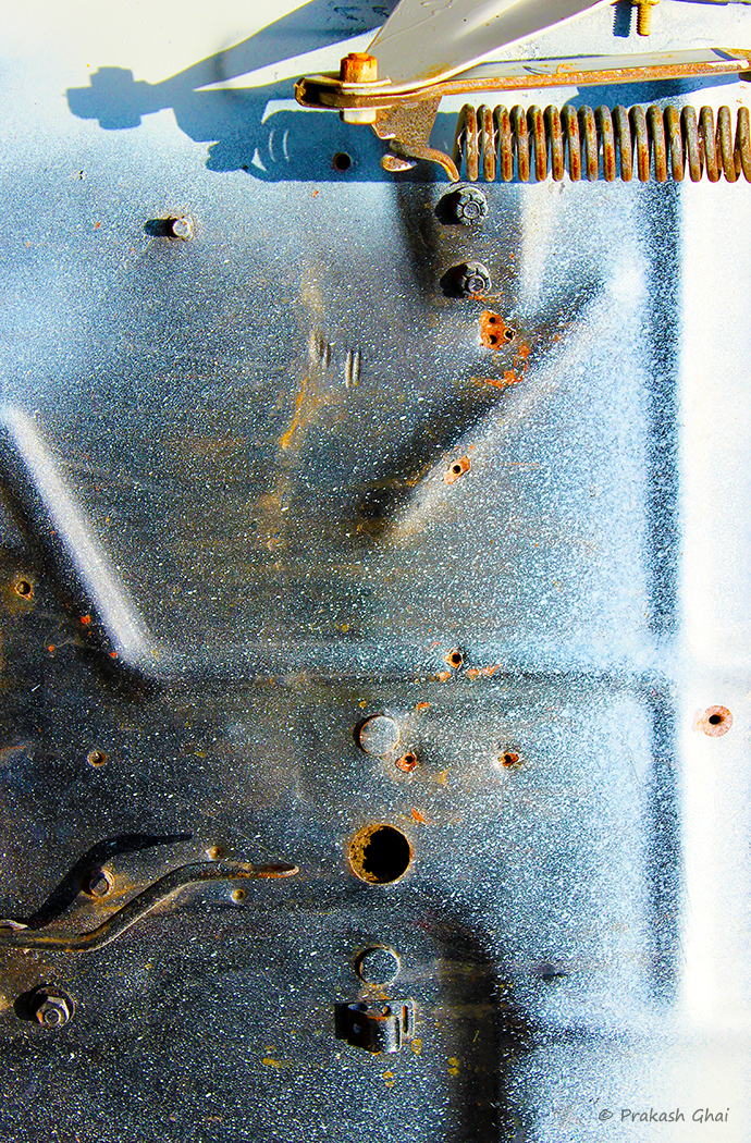 A Minimalist Photo of the Snippet of a blue metal sheet in an old car garage with a rusted spring on top.