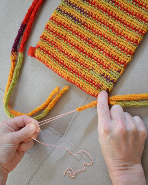 The left hand is pulling on both ends of the thread to pull the drawstring cords through the bead. The right hand is holding the bead still as the cords come through.