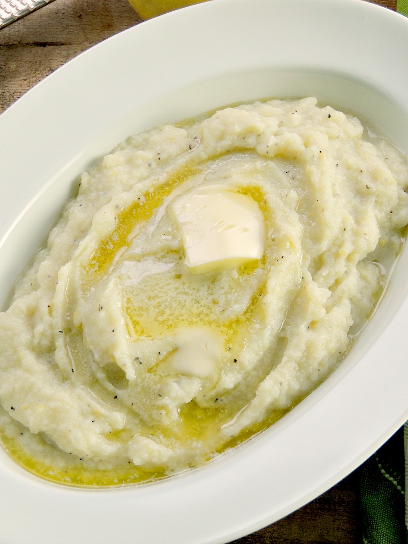 Lemon Garlic Mashed Cauliflower "Potatoes" topped with a pat of butter in a white bowl on a wooden background