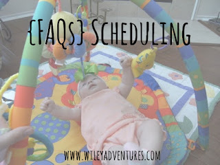 Text: FAQs Scheduling {Text in black on top of picture of baby girl on her back playing with a mobile toy