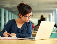 Bilgisayarına bakarak ders çalışan gözlüklü bir kız öğrenci