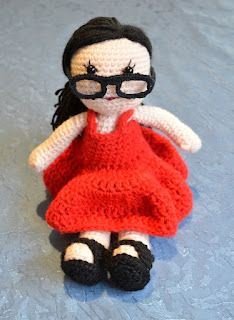 Front view of Kwokkie Doll seated, as she looks over the rims of her glasses.