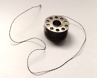 A metal sewing machine bobbin containing stainless steel thread. The plies of extremely fine stainless steel wire can be seen in the twist. The grey thread is as fine as a heavy duty sewing thread.