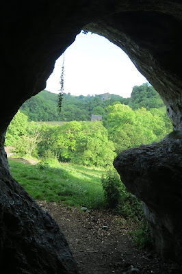 Looking out of a narrow cave entrance, Thor's Cave can be seen in the far distance above the trees.