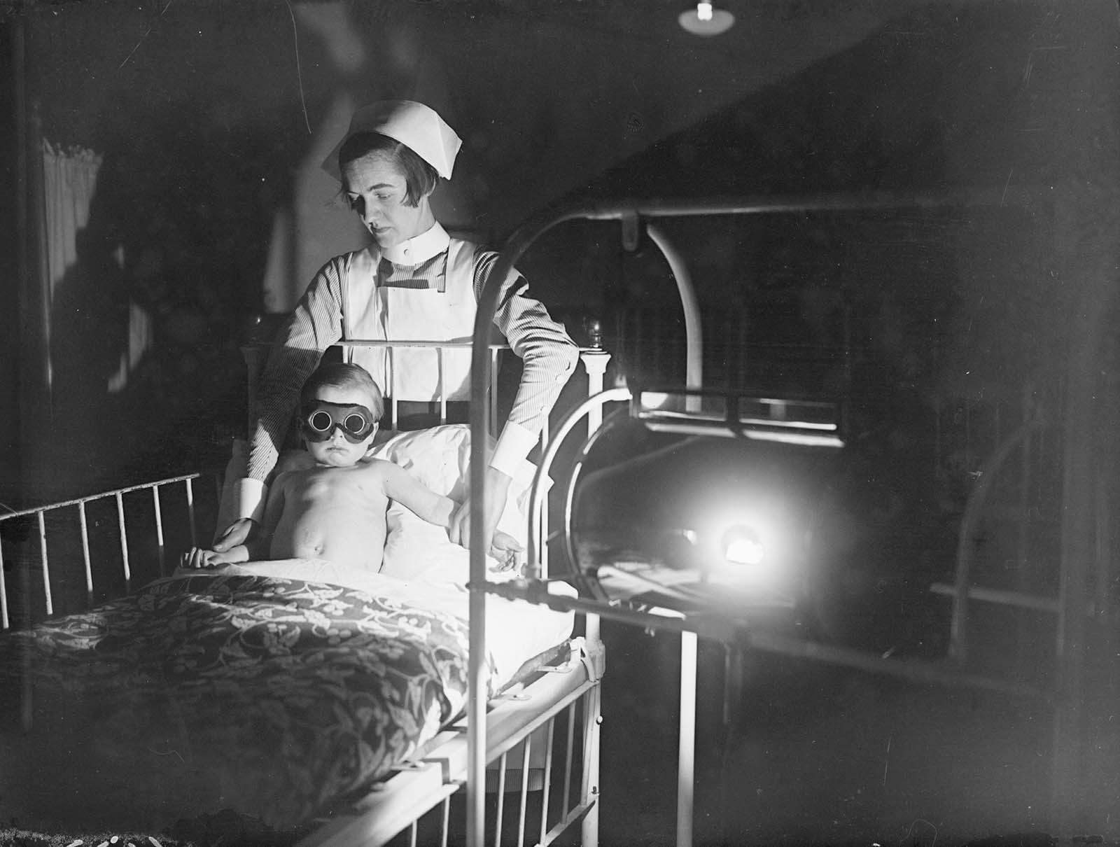 A child wearing goggles and held by a nurse, undergoes sun-ray treatment at Cheyne Hospital for Children, Chelsea. 1928.