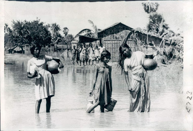 Girls+walk+through+flood+waters+on+a+road+near+Calcutta+(Kolkata)+as+they+carry+drinking+water+in+containers+from+distant+places+-+1959