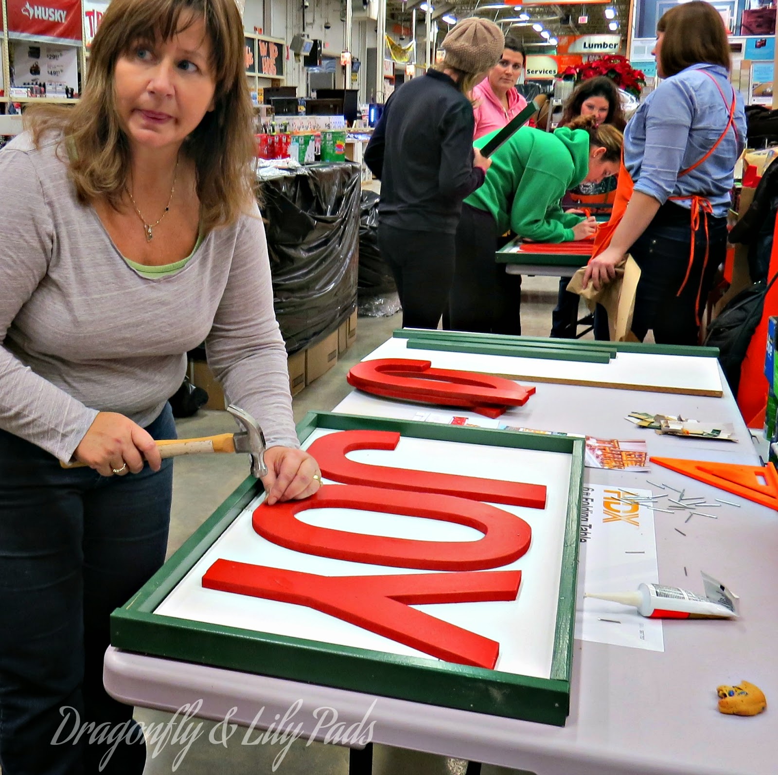 Women working at Her It Yourself Workshop in Home Depot Joy Marquee sign