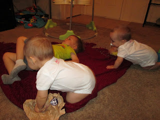 toddler boy laying on blanket while twin sister crawl on him to play