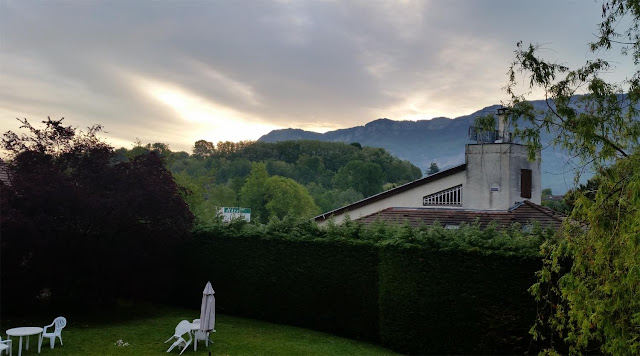 Blick in den Garten des Hotels mit weißen Plastikstühlen und im Hintergrund Berge mit Nebel und dezenten Sonnenaufgang