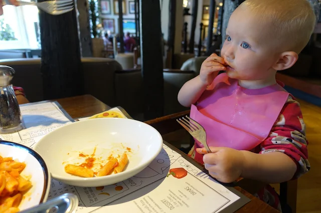 A toddler with a pink bib on sitting in a highchair in Prezzo eating pasta