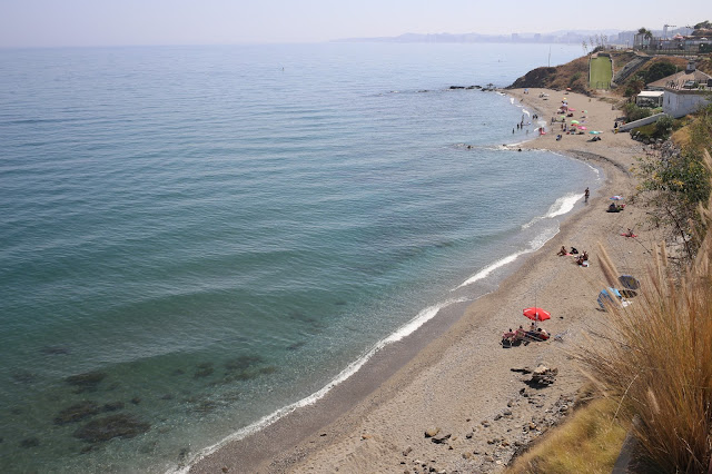 Playa estrecha vista desde arriba con las azules aguas del mar a su frente y acantilados a su espalda.