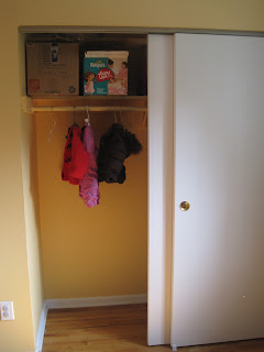 Open closet with just three items hanging, and two large boxes on the top shelf