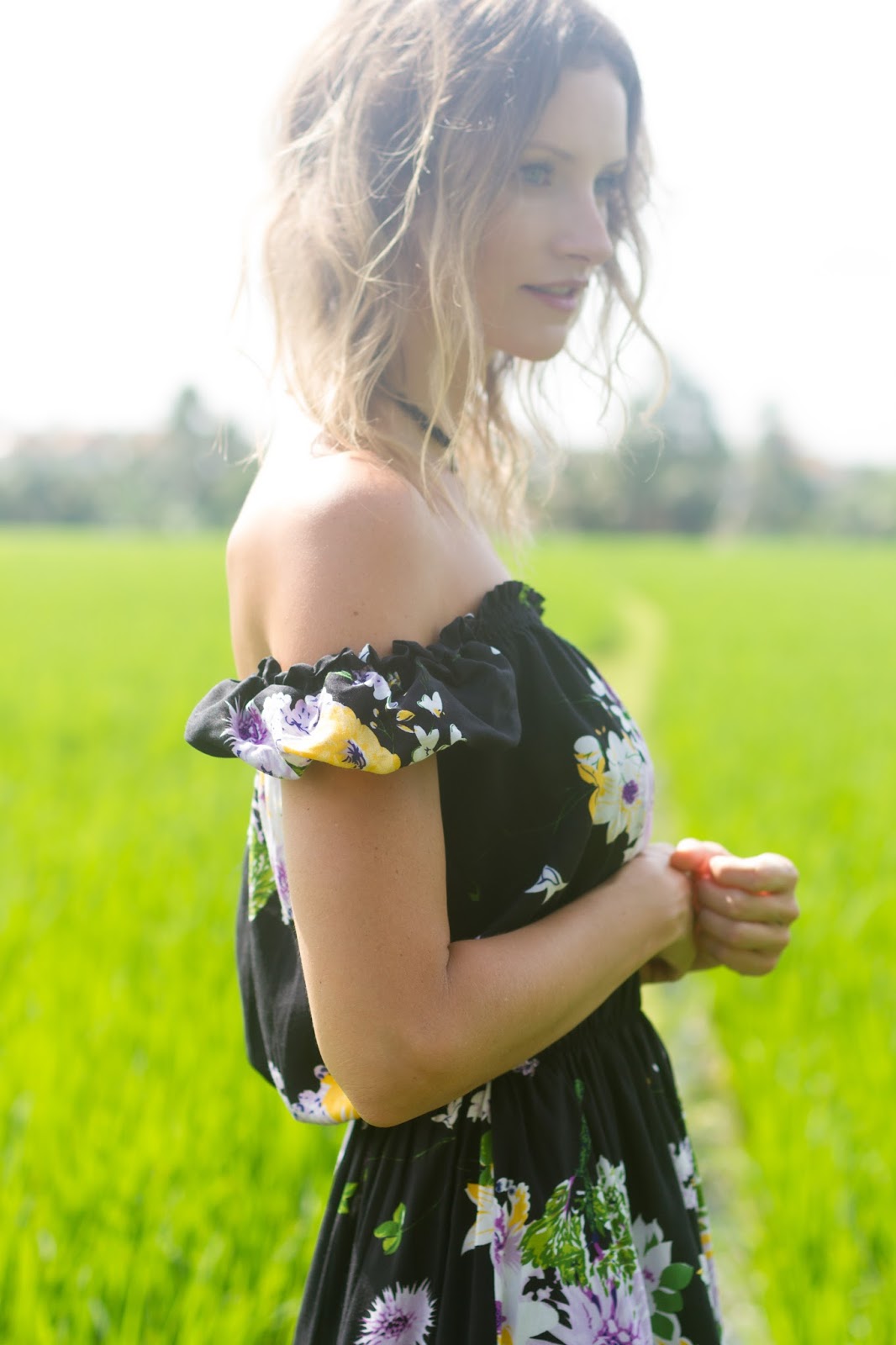 fashion and travel blogger, Alison Hutchinson, i s wearing the KAYVALYA Rosie Off The Shoulder Dress in Black Floral in a rice field in Bali