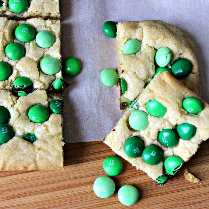 Mint M & M Sugar Cookie Bars on a board, cut into squares studded with green mint M&Ms