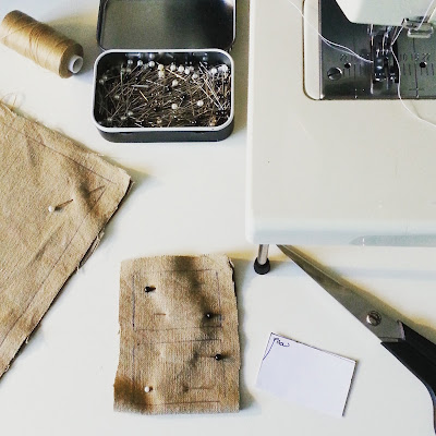 Tin of pins, sewing scissors, reel of thread and a sewing machine next to a pattern piece for a miniature pillow and two pinned and marked pieces of fabric.