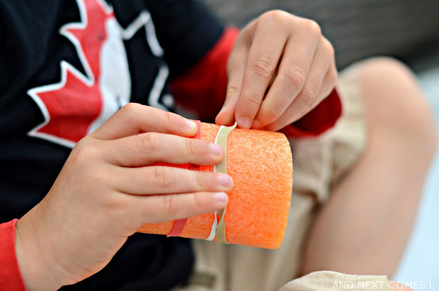 Child placing rubber bands on a pool noodle as a fine motor play idea