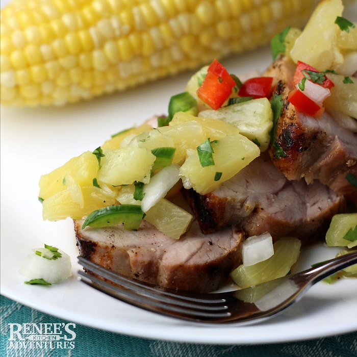 Grilled Pork Loin with Pineapple Salsa by Renee's Kitchen Adventures served on a white plate, with a fork and an ear of corn on the cob