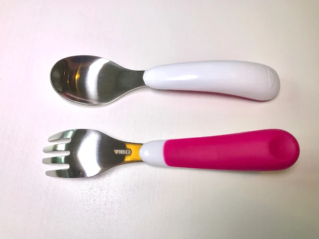 A fork and a spoon with metal ends and plastic handles. The top half is white and the lower half is pink silicone