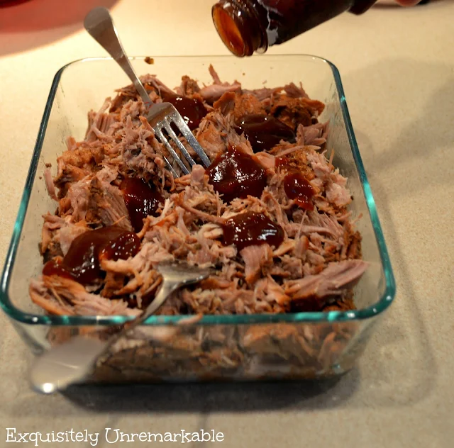 Shredded pork , barbeque sauce and two forks in a glass dish