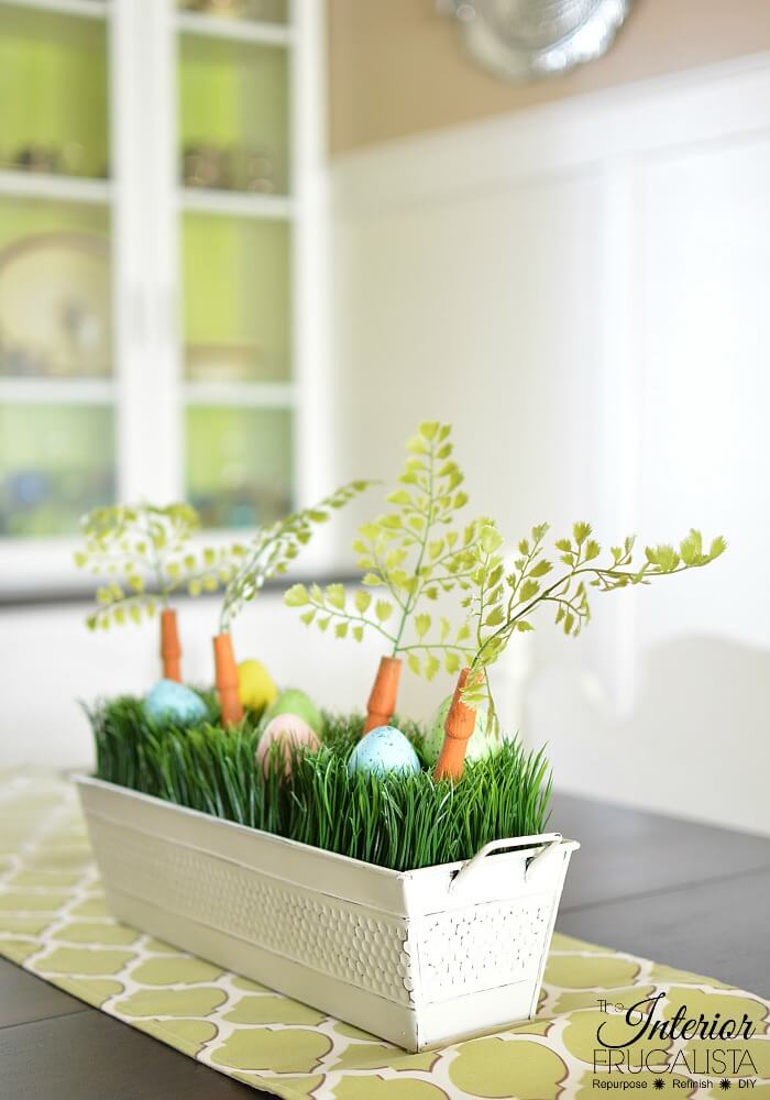 An upcycled Easter centerpiece box with faux wheatgrass, chair spindle carrots, and DIY speckled eggs for a fun budget Easter table decoration idea.