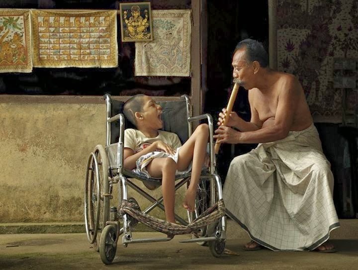small boy in wheelchair, man crouched down, playing flute for the boy