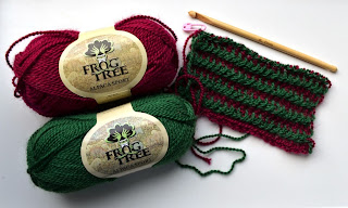 Two skeins of Frog Tree Alpaca Sport 100% alpaca yarn next to my scarf in progress which is made of alternating green and dark red stripes. The bamboo crochet hook is alongside the scarf in the top right hand corner of the photograph.