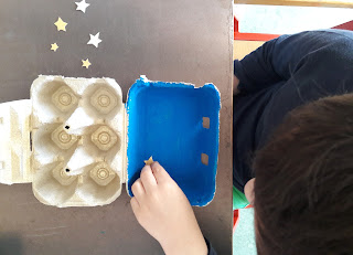 Um aluno a enfeitar o presépio com estrelas feitas em papel dourado