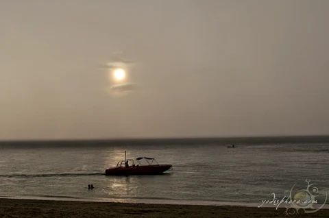 Boat cruising against a romantic sunset and rain at Puerto Galera white beach.