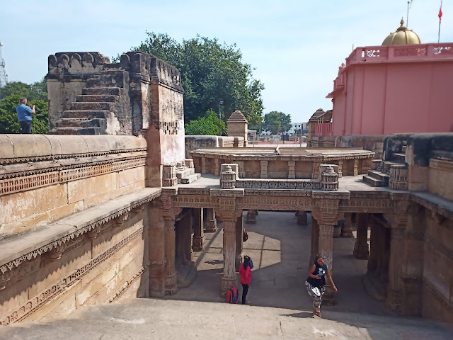 Stone stairs leading down into Adalaj Stepwell behind pink Hindu temple with gold dome