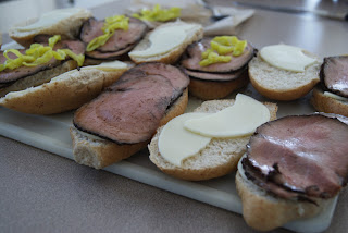 Sliced hoagies topped with sliced cheese, and beef, along with spicy mustard on a cutting board.