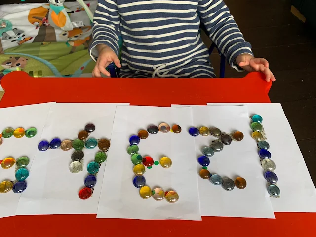 A toddler next to numbers 1 to 5 with glass nuggets tracing the numbers
