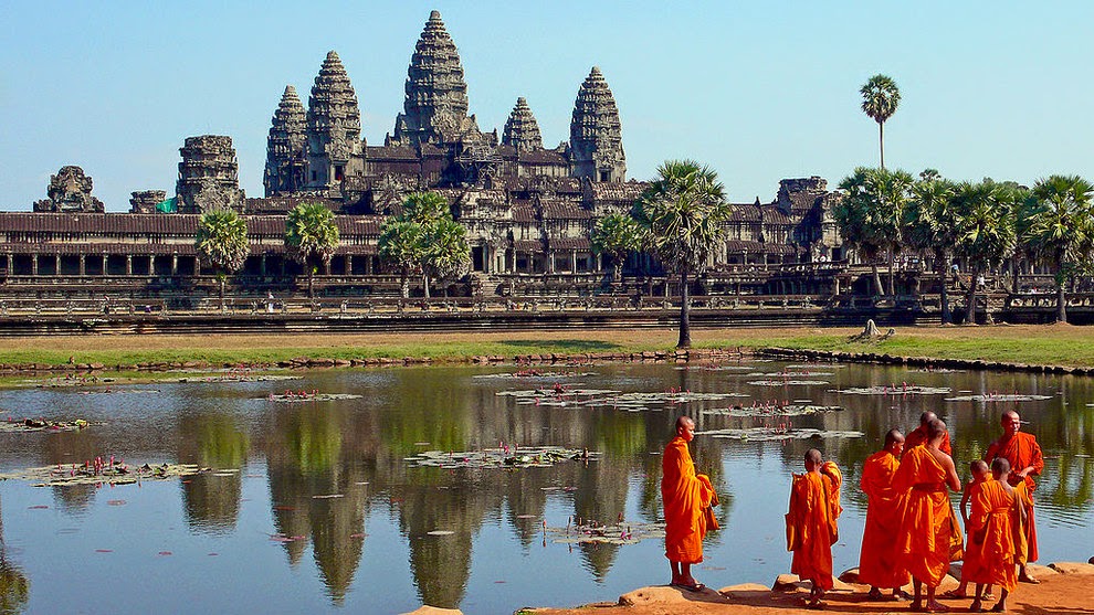 monjes reunidos al lado de un lago y al fondo los restos de una civilizacion pasada