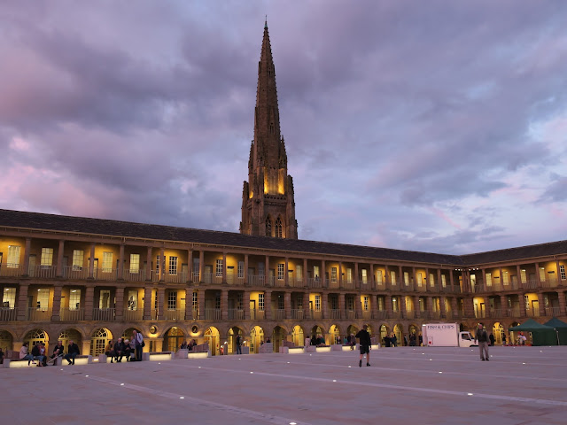 Halifax Piece Hall at night with people looking round and Spire beside Square Chapel Beyond.