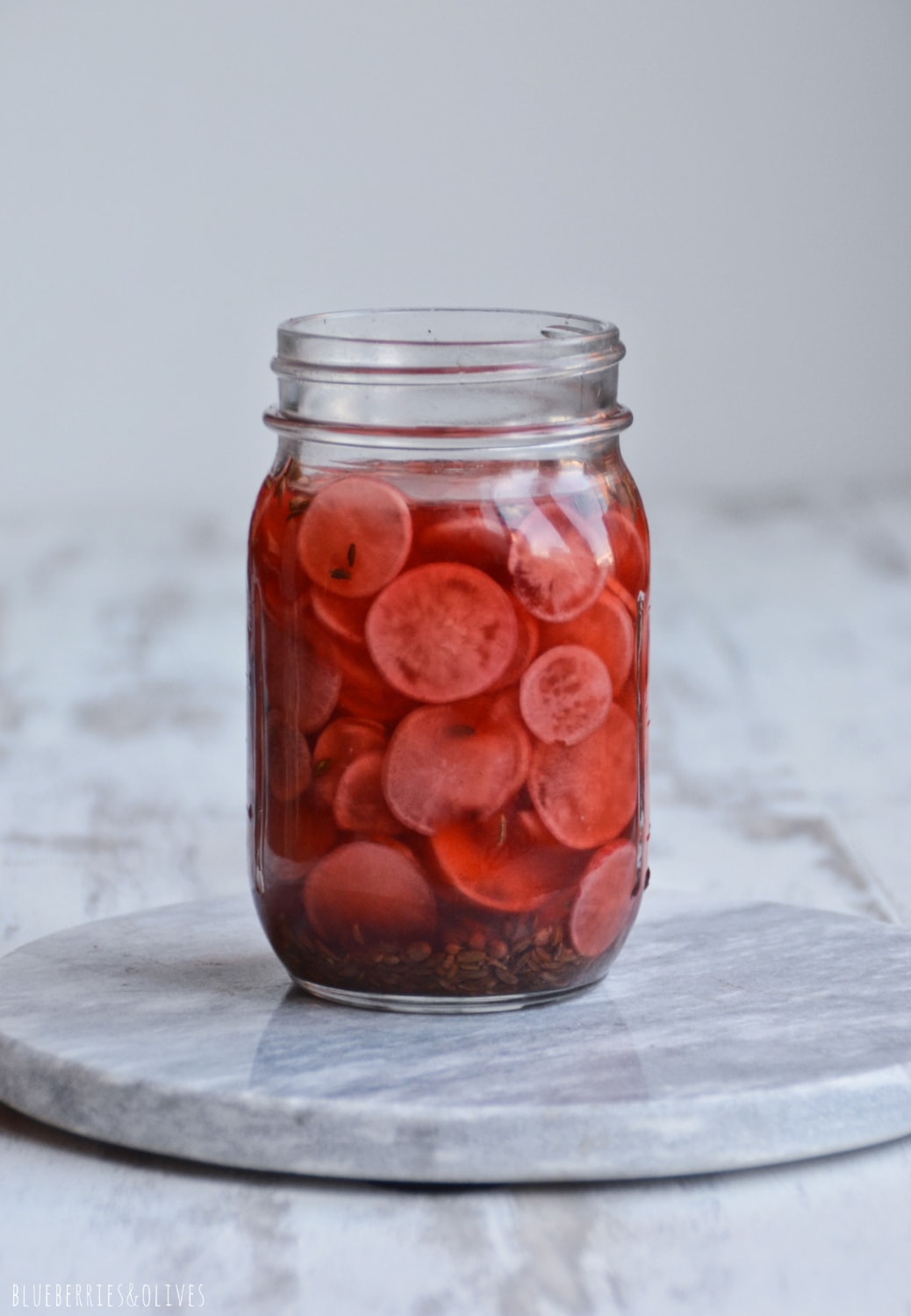 PICKLED RADISHES IN A GLASS JAR, WHITE MARBLE CUTTING BOARD AND WHITE BACKGROUND