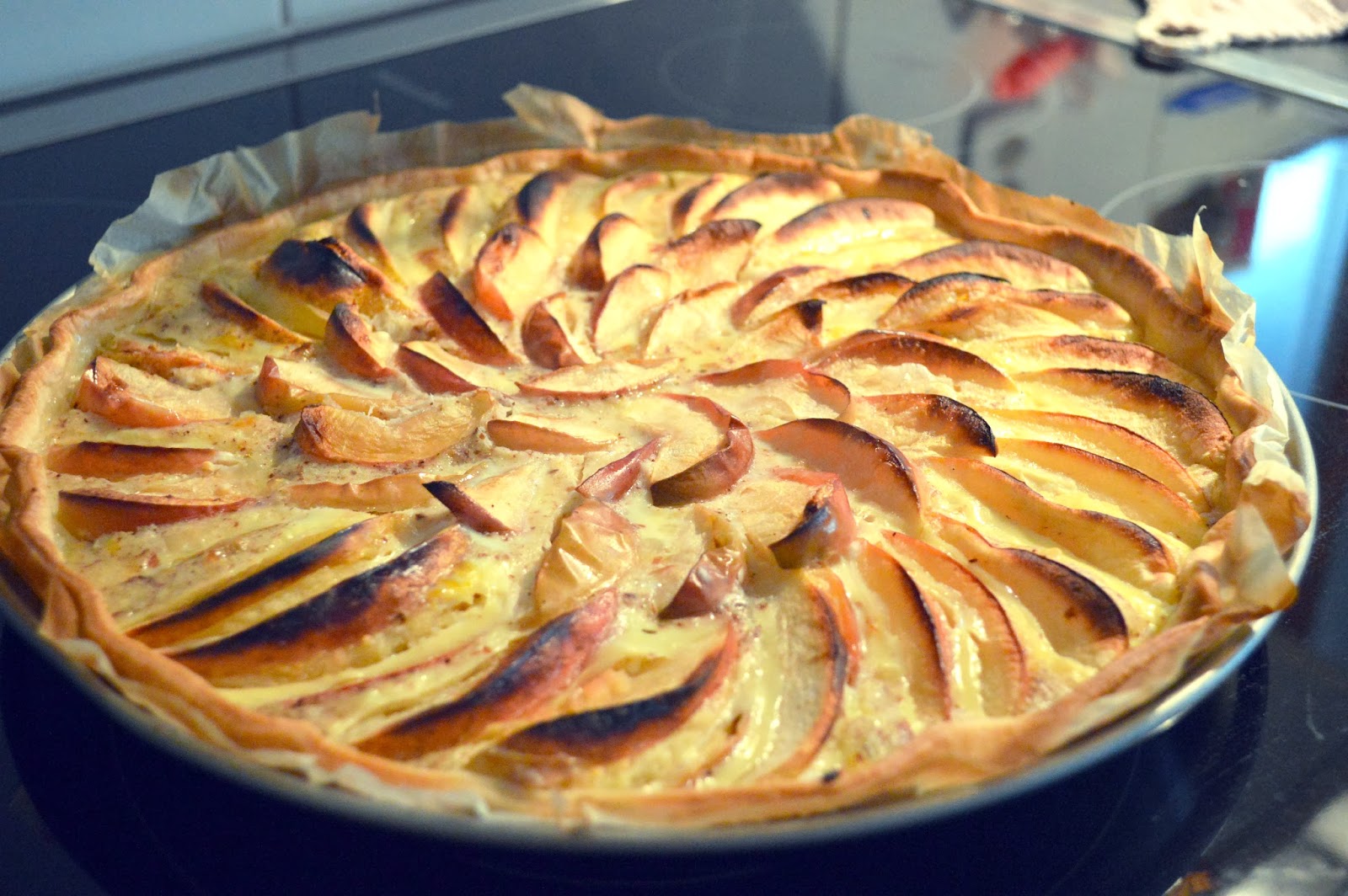 The image show a large round pastry with a lattice top and cut apple slices in a round pattern
