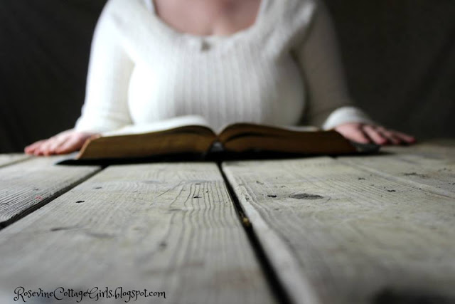What are we letting beat us - Woman reading her bible at a rough hewn wooden table.
