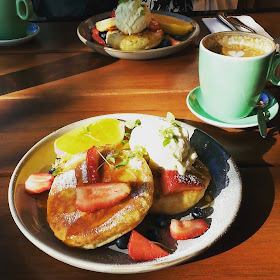 Plate of hotcakes and fruit, next to a mug of coffee at a cafe.