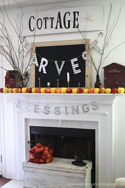Photo of a mantel with red and yellow apples, harvest metal sign, blessings metal sign. White sign with the word Cottage and black chalkboard | rosevinecottagegirls.com |Minimalist Farmhouse Apple Mantel