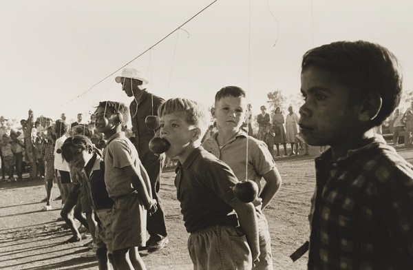 Mervyn Bishop, "Town picnic, Brewarrina", 1966. Vintage foto australia: niños juegan a comer manzanas que cuelgan de un lazo. Dia de campo actividades.